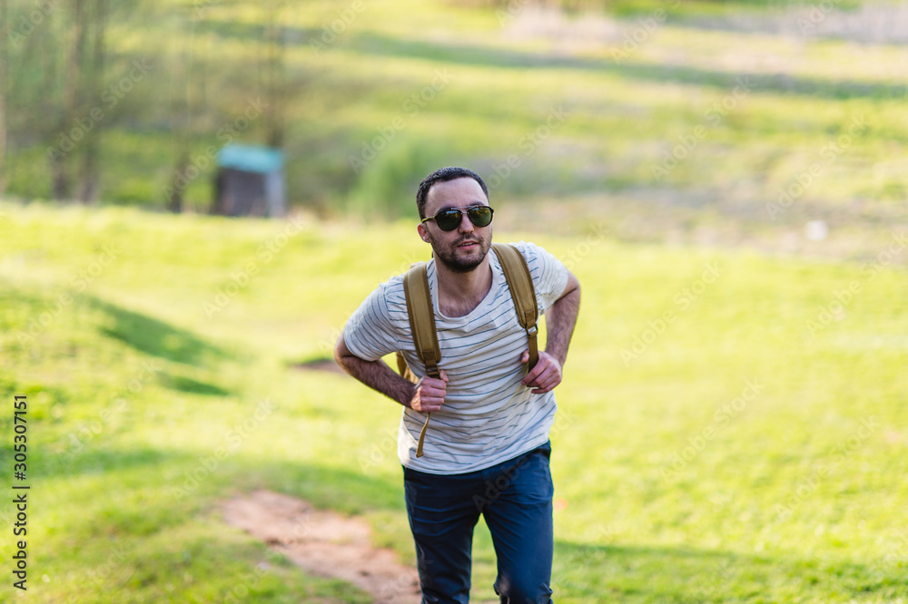 Hiking man portrait with backpack walking in nature. Caucasian man smiling happy with forest in background during summer trip Hiking man portrait with backpack walking in nature. Caucasian man smiling happy with forest in background during summer trip