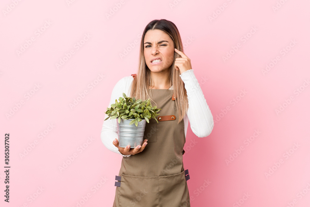 Young gardener woman holding a plant covering ears with hands. Young gardener woman holding a plant covering ears with hands.