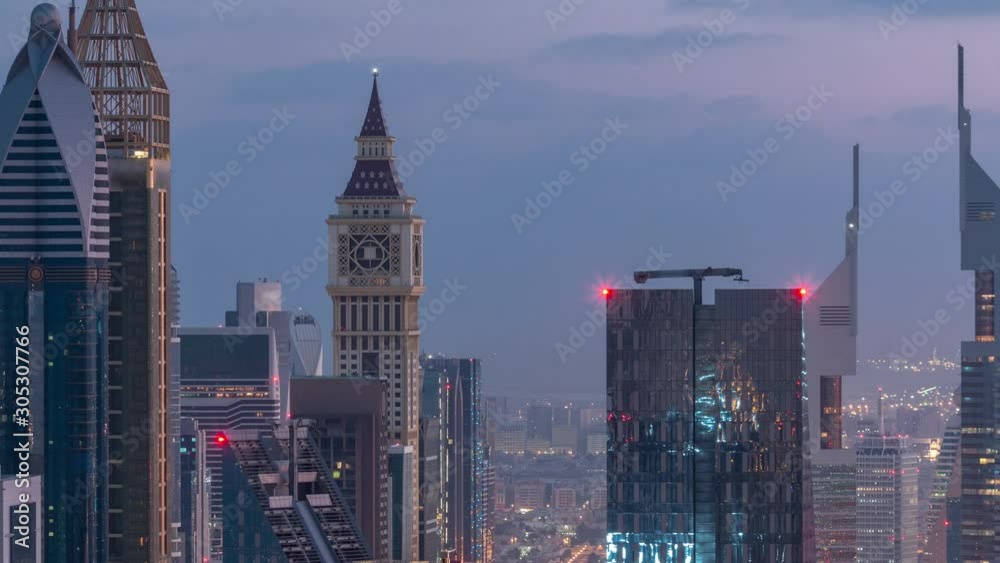 Dubai International Financial Centre district with illuminated modern skyscrapers night to day transition timelapse. Aerial view from Downtown with traffic on streets before sunrise