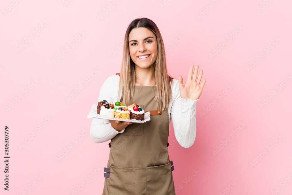 Young baker woman holding sweets smiling cheerful showing number five with fingers. Young baker woman holding sweets smiling cheerful showing number five with fingers.