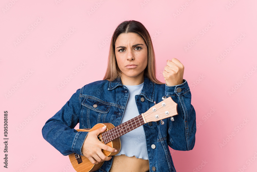 Fototapeta premium Young caucasian woman playing ukelele showing fist to camera, aggressive facial expression.