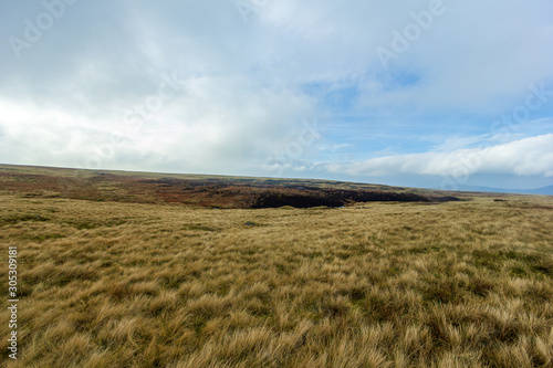 A view of a grassy mountain plateau with bog in the background unde a cloudy blue sky