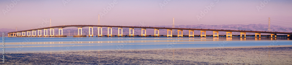 Panoramic view of San Mateo Bridge at sunset; electricity towers and power lines visible behind it; the San Mateo Bridge is connecting the Peninsula and East Bay in San Francisco Bay Area, California Panoramic view of San Mateo Bridge at sunset; electricity towers and power lines visible behind it; the San Mateo Bridge is connecting the Peninsula and East Bay in San Francisco Bay Area, California