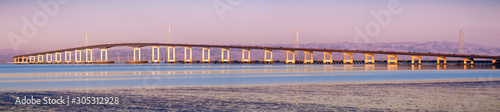 Panoramic view of San Mateo Bridge at sunset; electricity towers and power lines visible behind it; the San Mateo Bridge is connecting the Peninsula and East Bay in San Francisco Bay Area, California