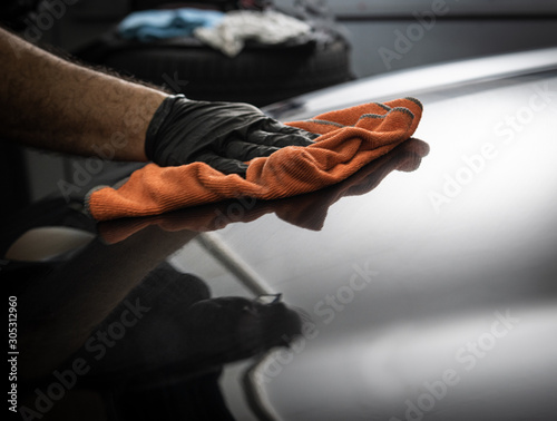 car wash - polishing a car with an orange cloth and a male hand with a black glove shining the hood of a car where the light is reflecting 