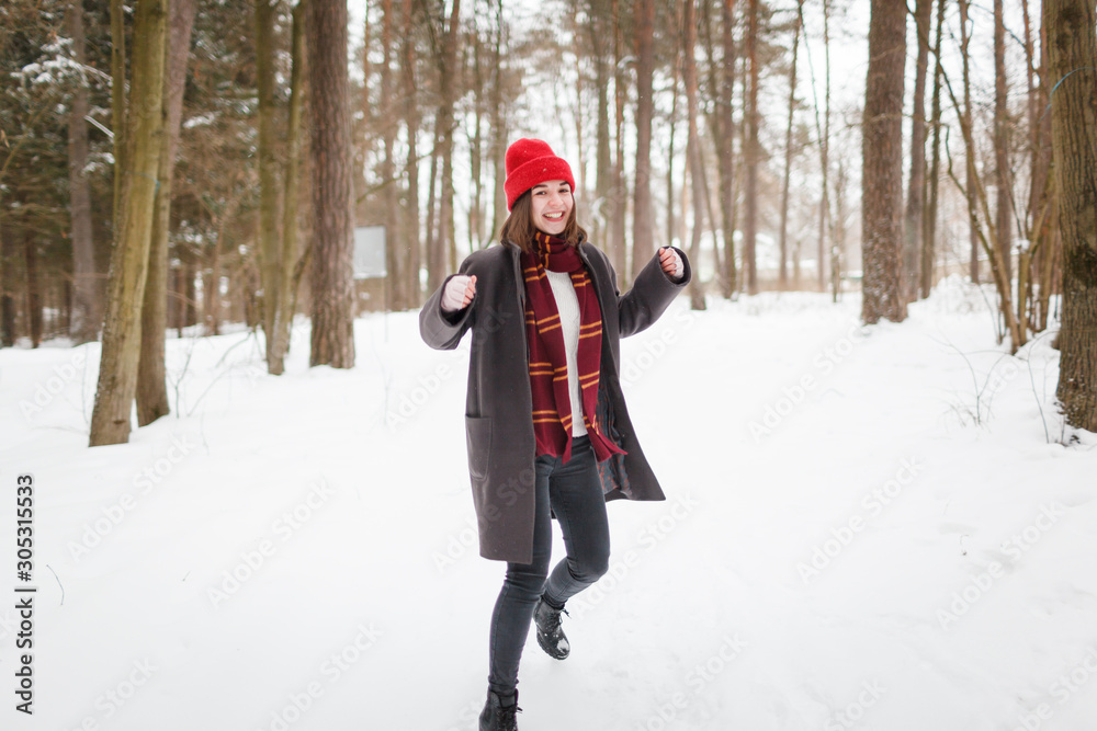 Young woman with brown hair and gryffindor scarf is dancing in winter forest