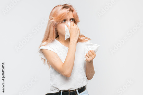 Studio portrait of young blonde woman blowing her nose into a paper napkin. The epidemic of cold, sneezing, allergy symptoms, flu, rhinitis, sickness, desperately sick. Healthcare and medicine concept