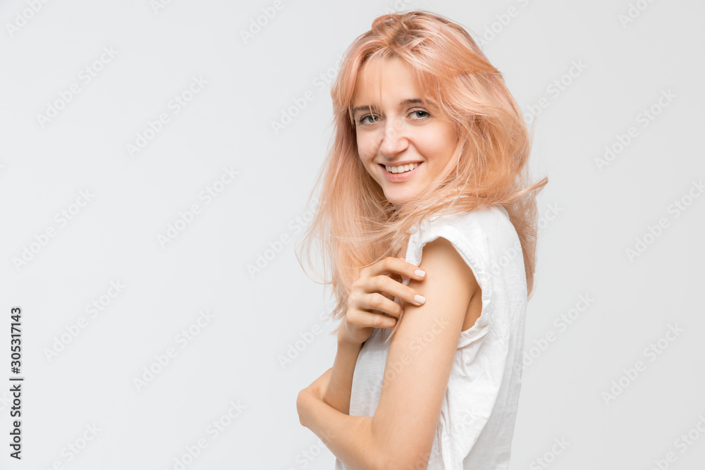 Side view portrait of cute attractive blonde girl in white t-shirt. Woman crossed her arms over her chest, look at camera and smile. Good-looking cheerful female. Youth and beauty concept. Copy space.