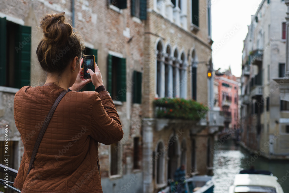 Beautiful girl traveler photographs the streets and canals of Venice on her smartphone.