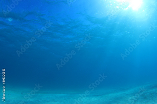 Underwater photo of blue ocean, sunbeams and sandy sea floor