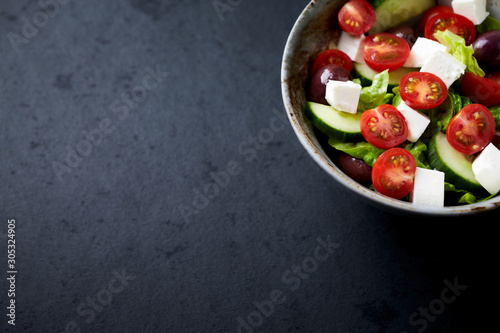 Salad with Kalamata Olives, Cucumber Cherry Tomatoes and Feta Cheese on black Stone Background. Healthy Snack Idea. Close up.