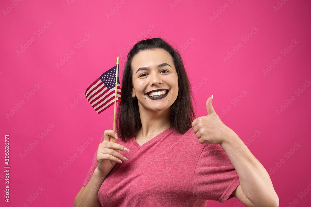 Happy young woman holding American flag against a studio pink background Happy young woman holding American flag against a studio pink background