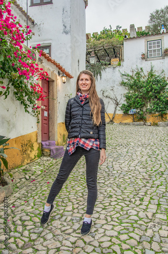 A woman walks through the streets of the old town of Obidos in Portugal. Trees, flowers, houses, autumn.