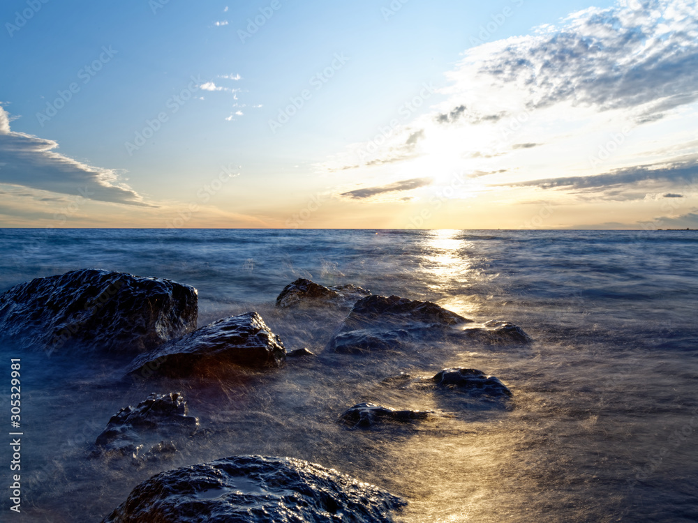 Obraz premium Hazy water over shoreline rocks near sunset. 