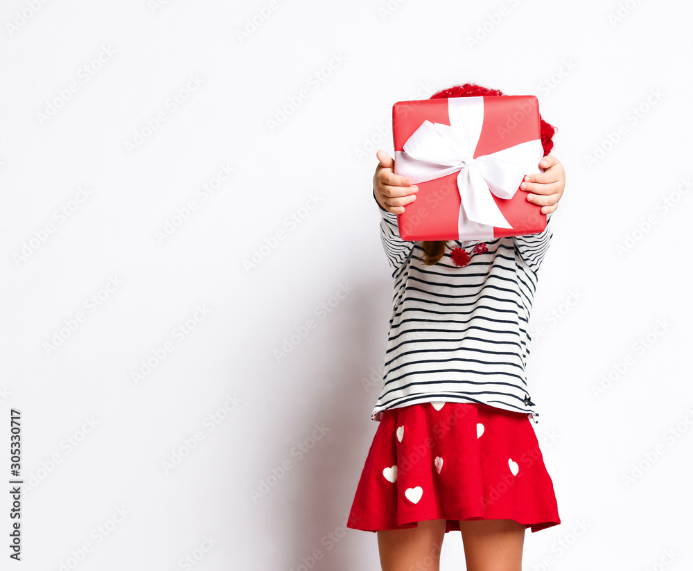 Fototapeta premium Happy cute young girl holding a red gift box with a white ribbon over a light background