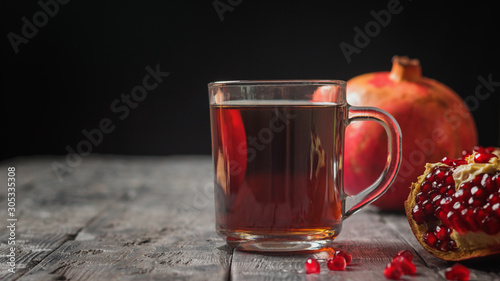 Glass mug with pomegranate juice and fresh pomegranates on a wooden table.