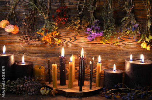 Still life with burning candles and dry herbs on witch table.