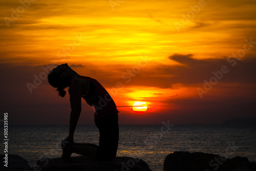 Silhouette woman is play yoga excercise on stone near the beach with sunset time