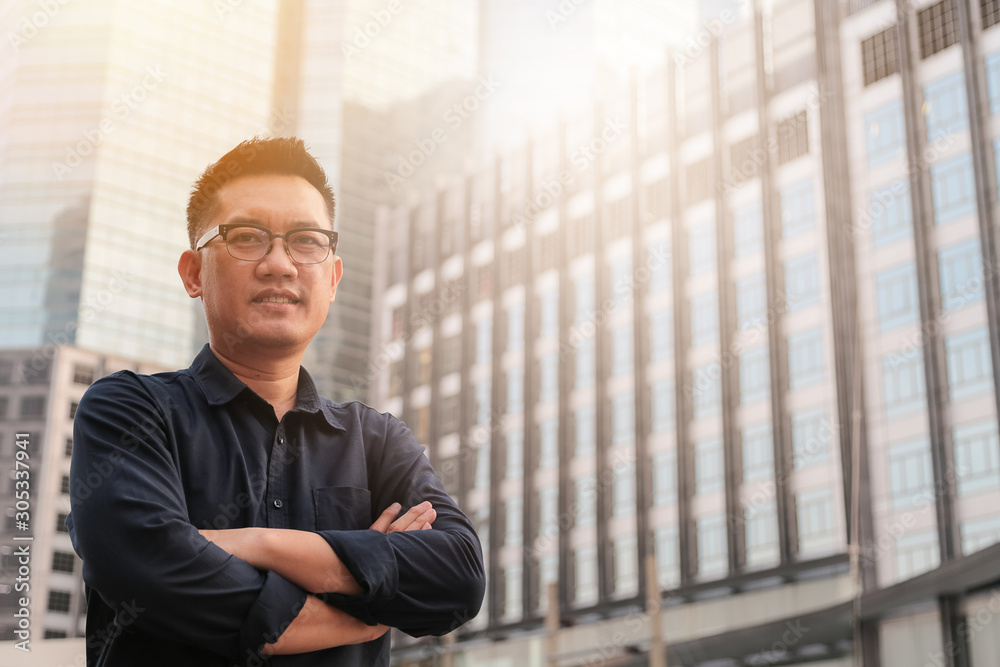 Fototapeta premium Confident male business executive with arms crossed standing in front of office building