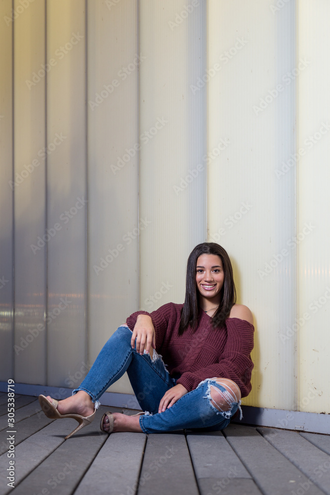 Full length of mixed raced teenage girl sitting next to a white wall smiling