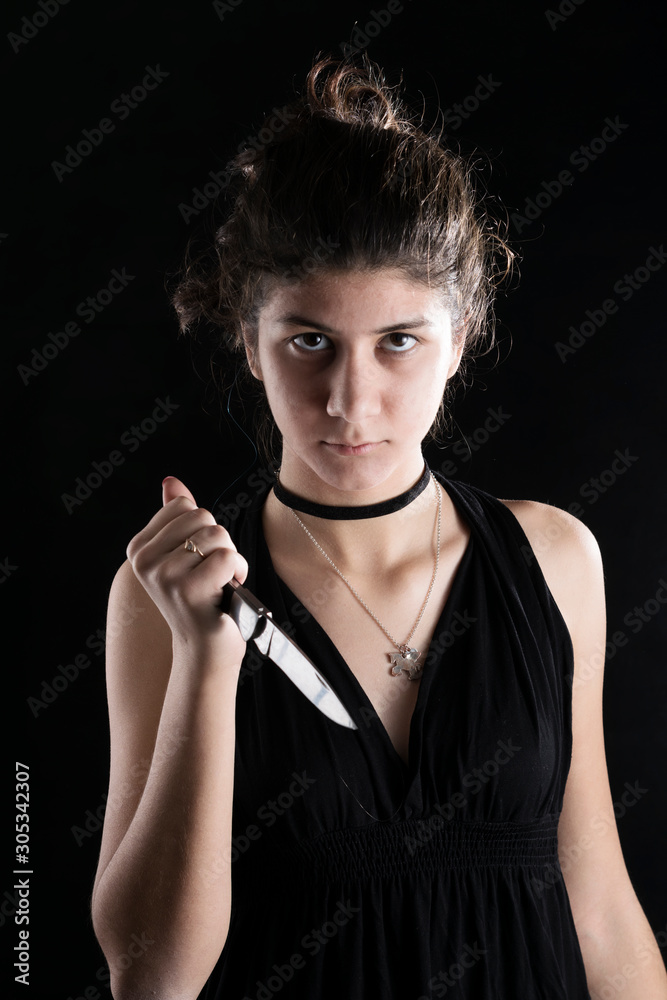 Obraz premium Teenager girl threateningly holds a small knife in his hand. Concept of protection against domestic violence. On a black background.