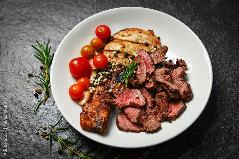 Roasted beef steak fillet and pork chops with herb and spices serve with vegetable on white plate - grilled beef meat slice on black background