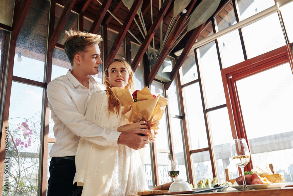 Handsome young man hugging smiling girlfriend with bouquet of flowers Handsome young man hugging smiling girlfriend with bouquet of flowers