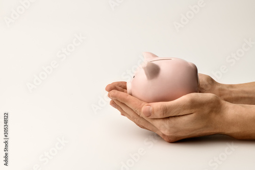 In men's hands lies a pink piggy Bank on a gray background. A fragment of a man's hands