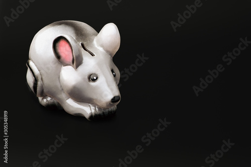 Piggy Bank in the form of a gray mouse or rat sits on a black background .