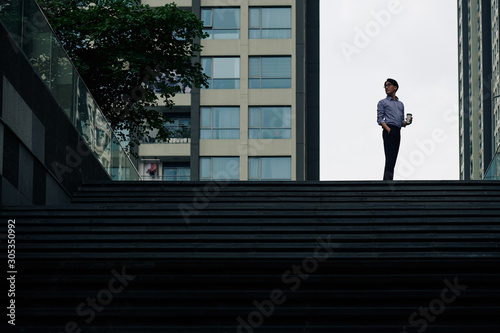 Man with cup of take away coffee standing on top of the stairs and turning back to look at his office building