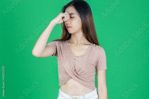 Exhausted stressed young Asian woman with hands on face feeling disappointed on green isolated background.