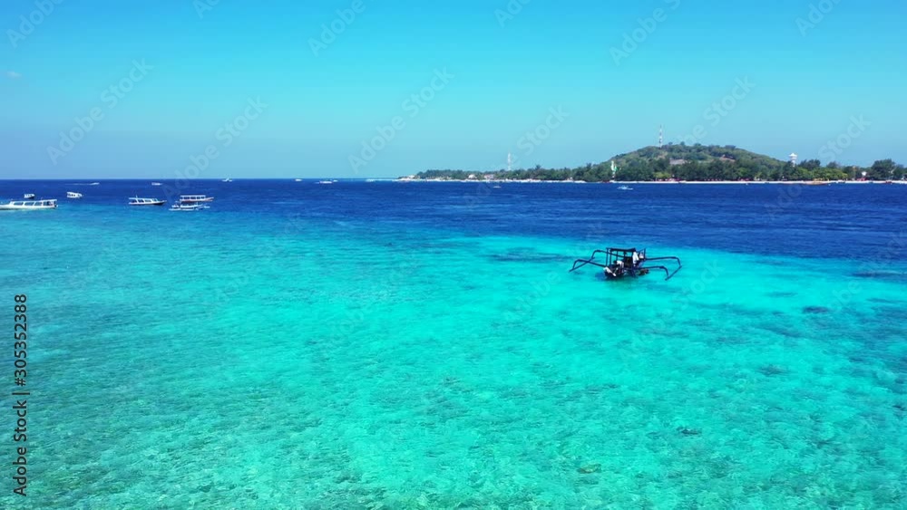 Gili trawangan Island - Man In A Floating Boat On A Bright Blue Sea Water With Lush Island In The Background - Wide Shot Gili trawangan Island - Man In A Floating Boat On A Bright Blue Sea Water With Lush Island In The Background - Wide Shot