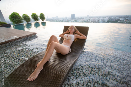 Young woman enjoying a sun, Slim young girl model in white bikini by the pool.