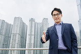 Smiling Asian businessman outstretching hand for handshake, skyscrapers in background