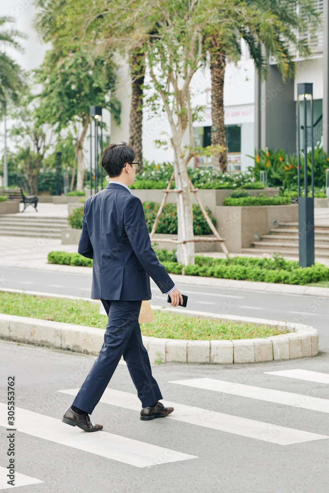 Businessman in suit carrying paper package with lunch and crossing road