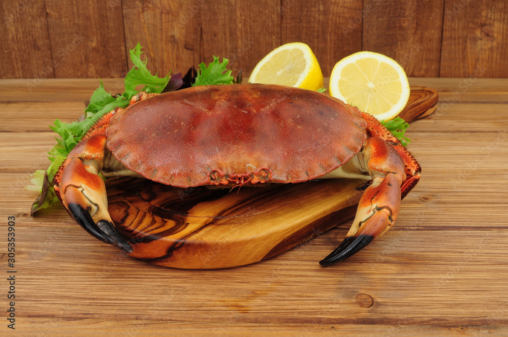 Whole fresh cooked brown crab on a wooden background with lemon and salad leaves Whole fresh cooked brown crab on a wooden background with lemon and salad leaves