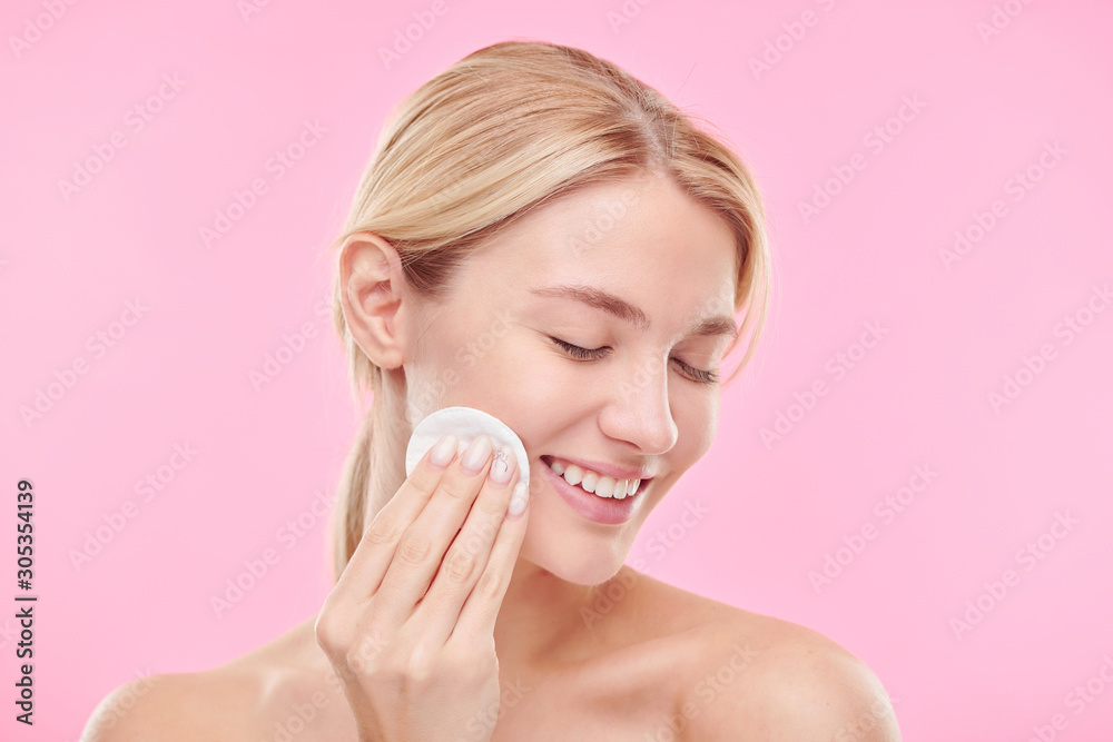 Pretty young smiling female with cotton pad enjoying procedure of cleaning face Pretty young smiling female with cotton pad enjoying procedure of cleaning face