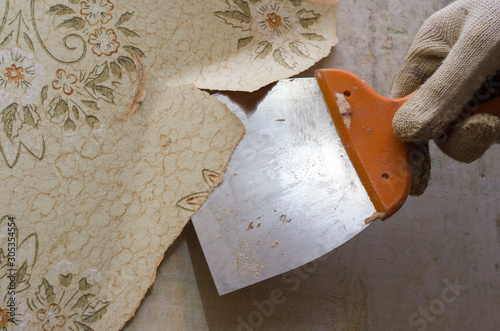 Preparing the wall for painting or sticking new wallpaper. Man in gloves with a scraper in the process of removing old wallpaper. wetted with a special solution surface photo