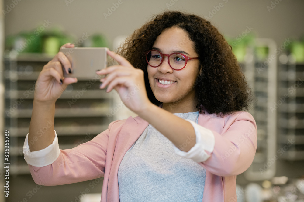 Happy intercultural girl in eyeglasses holding smartphone in front of her face Happy intercultural girl in eyeglasses holding smartphone in front of her face