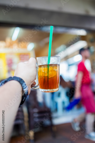 Hand holding ice tea in a glass with straw