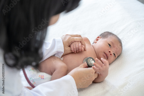 Adorable asian newborn baby girl check up examines by pediatrician doctor. Female doctor hand using stethoscope examining little cute baby infant heart and lung in clinic. Baby health care concept.
