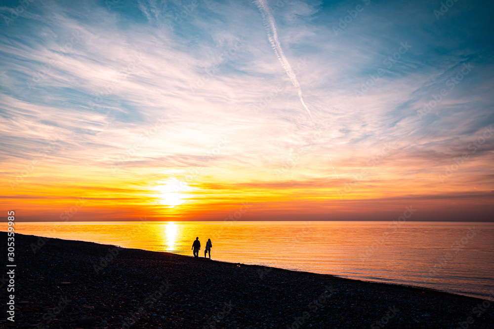 Silhouettes of loving couple walking along the seashore at sunset