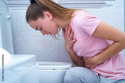Foto Young woman suffers from nausea and vomiting due to digestive and stomach illness problems at bathroom