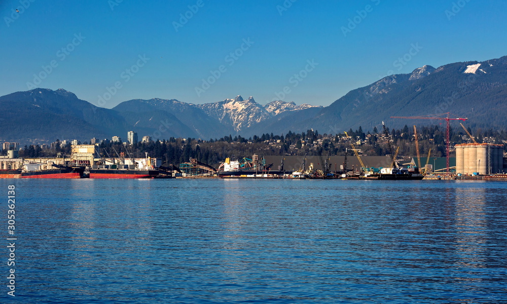  The ships under loading in the sea port of North Vancouver on the   background of mountain range and blue sky