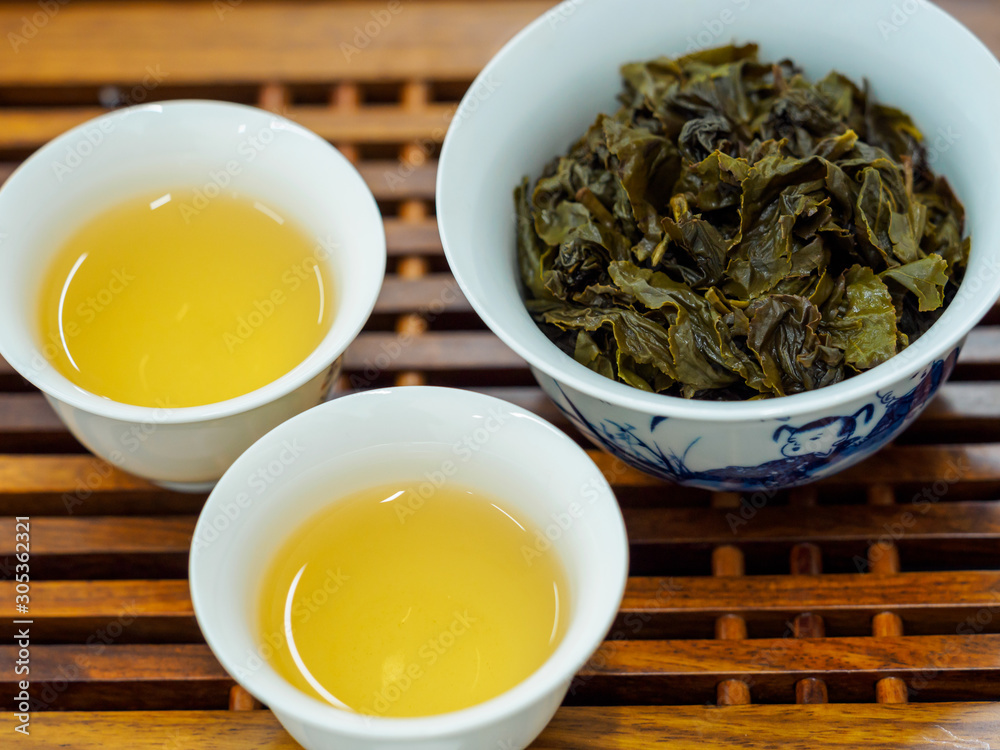 High angle view of cups of green oolong tea and tea leaves on a wooden tray