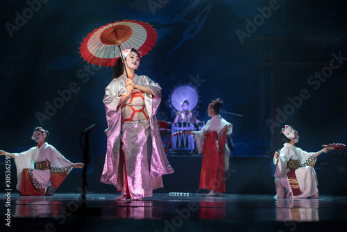 Traditional Japanese performance. Actresses in traditional white and red kimono and fox masks dancing with umbrella and fans.