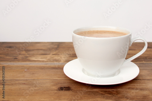 cappuccino coffee in a white cup and saucer with copy space on an old wooden table, concept of a stylish cafe
