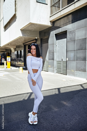  Attractive fitness woman posing on city street.Beautiful young sports woman relaxing and having rest after training outdoors.Beautiful long female legs. Healthy girl wearing trendy sportswea photo