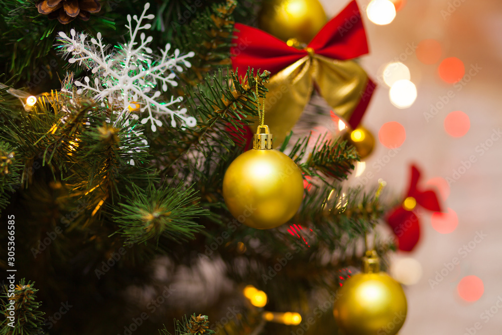 Beautiful green Christmas tree decorated with yellow balls, red bows and garlands. Close-up photo. Sparkling background