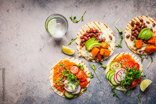 Open vegan tortilla wraps with sweet potato, beans, avocado, tomatoes, pumpkin and  sprouts on gray background, flat lay, copy space. Healthy vegan food concept. photo